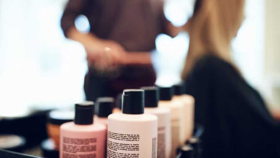 Hair salon with various hair care products in focus, stylist working in background.
