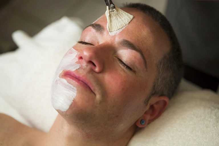 Man receiving a facial treatment with a brush applying a mask to his face.
