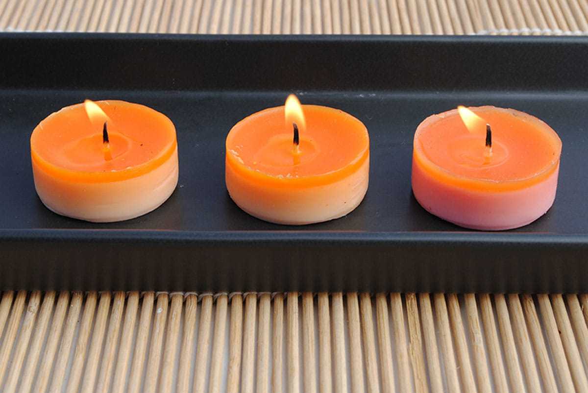 Three orange tealight candles burning on a black tray.